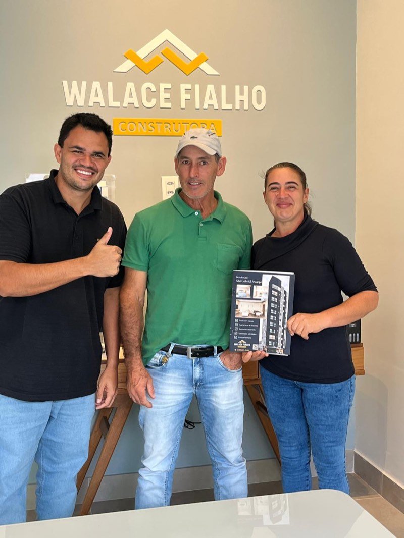 Compradores no stand de vendas segurando o material do Residencial São Gabriel Arcanjo, ao lado da vendedora.